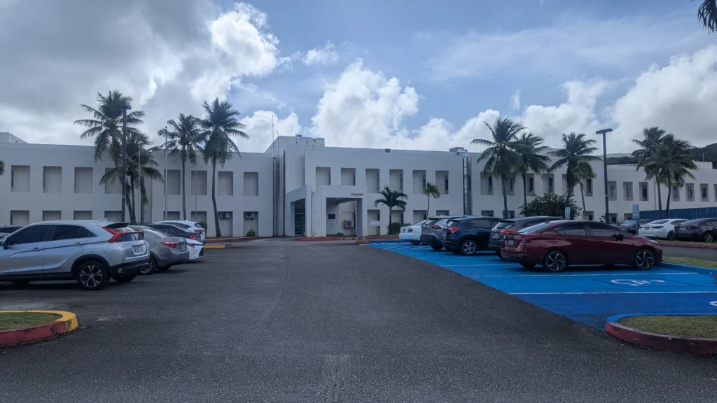 The Heart of Saipan's Healthcare. The Exterior of Commonwealth Health Center hospital building in Saipan with palm trees and parking lot in foreground.