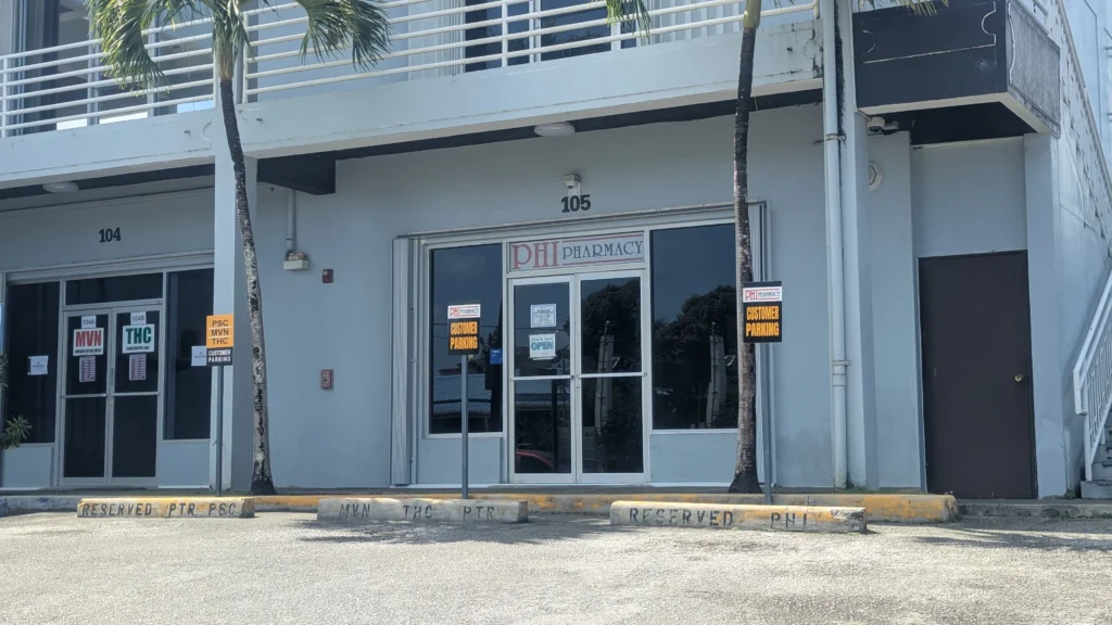 PHI Pharmacy storefront exterior in Saipan, CNMI with open sign visible in window.